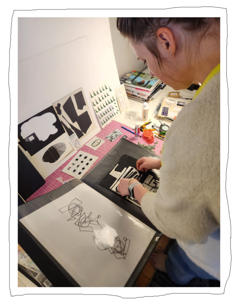 Artist Laura Kinney assembling a paper collage in her studio, surrounded by cut paper works in progress